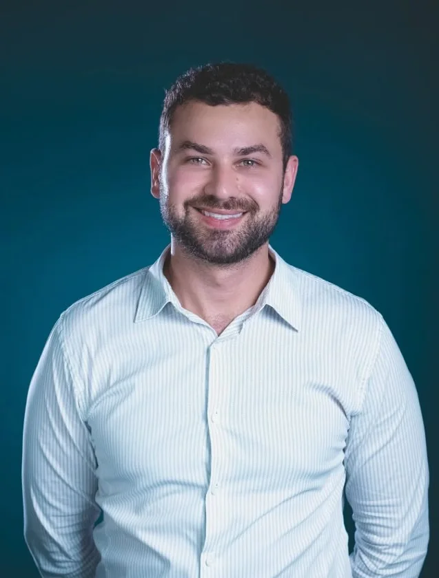 Retrato do Dr. César Giudice sorrindo, de camisa clara, em fundo azul petróleo